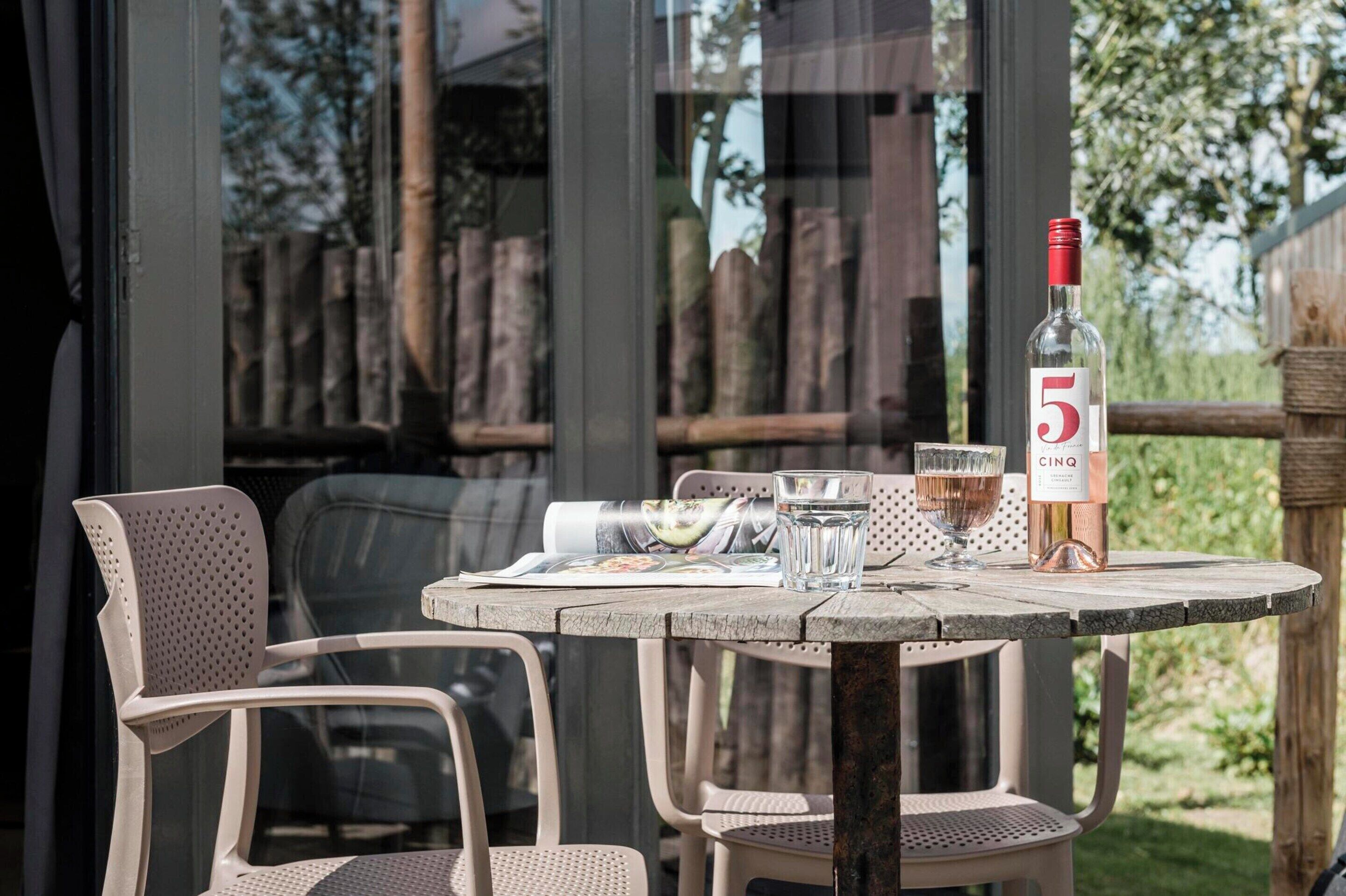 A round wooden table with a bottle of wine, two glasses, and a menu.