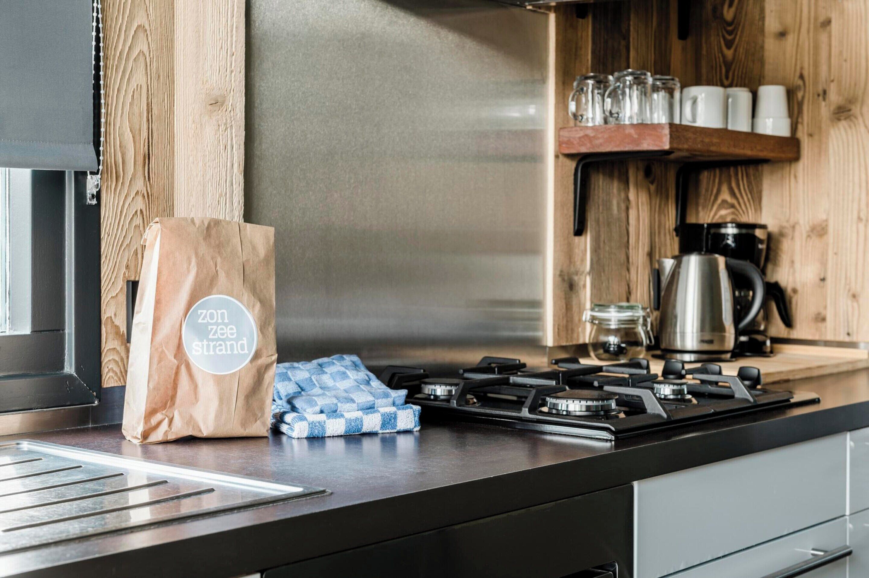 A kitchen with a gas stove, a coffee maker, and a shelf with cups and jars.