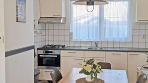 A kitchen with a dining table, chairs, a stove, oven, and a hanging light fixture. - Cosy Bungalow Near the Beach (Breskens)