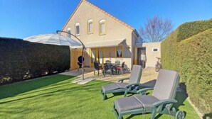 A house with a patio area featuring two lounge chairs and a table. - Cosy Bungalow Near the Beach (Breskens)