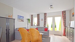 A living room with a sofa, two wicker chairs, a television, and a cabinet. - Cosy Bungalow Near the Beach (Breskens)