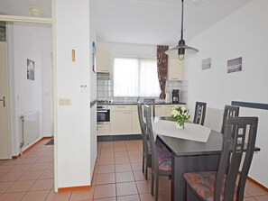 Une cuisine de taille réduite avec une table et des chaises, une fenêtre avec des rideaux et un radiateur fixé au mur.
