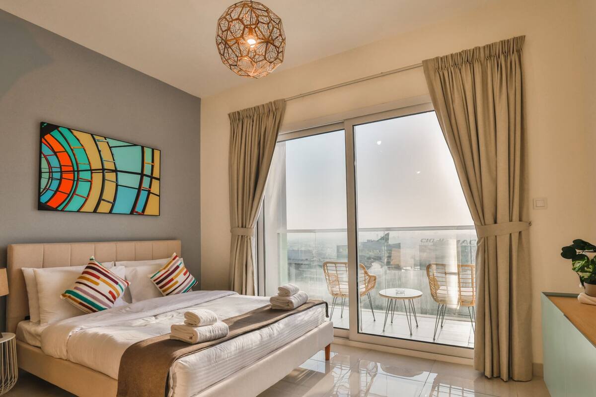 A modern hotel room with a large bed, a city view balcony, and a contemporary art piece.