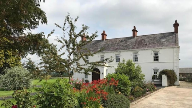 A white building with a grey roof, surrounded by a garden with various plants and flowers. - Flatfield Clocktower Cottages Self Catering By Belvilla (Craigavon)