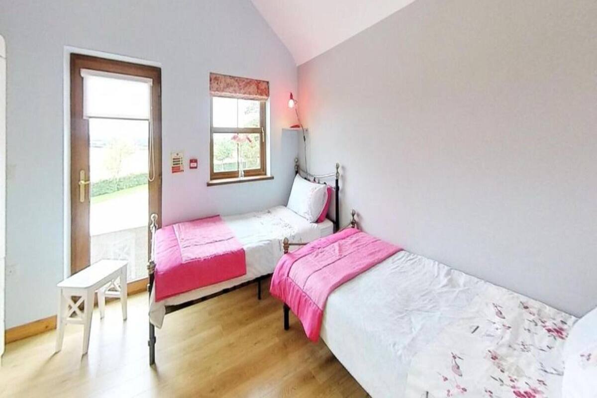 A bedroom with two single beds, a small white desk, and a window with a view of greenery.