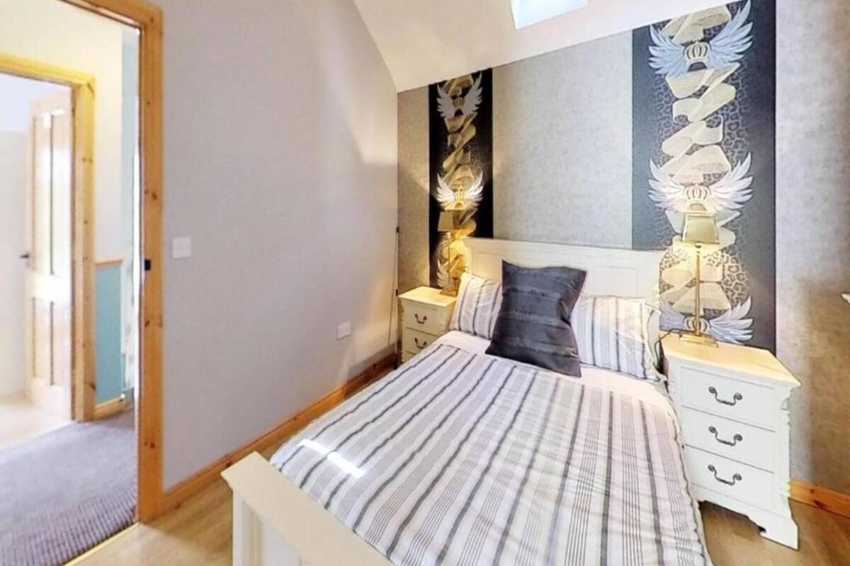 A bedroom with a bed, nightstands, a lamp, and a wall with a decorative design.