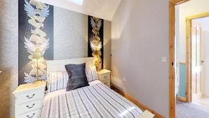 A bedroom with a bed, two bedside tables, a lamp, and a wall with a decorative design. - Flatfield Clocktower Cottages Self Catering By Belvilla (Craigavon)