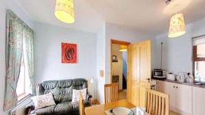 A living room with a sofa, a dining table with chairs, a kitchen area with a microwave, and a staircase leading to another room. - Flatfield Clocktower Cottages Self Catering By Belvilla (Craigavon)