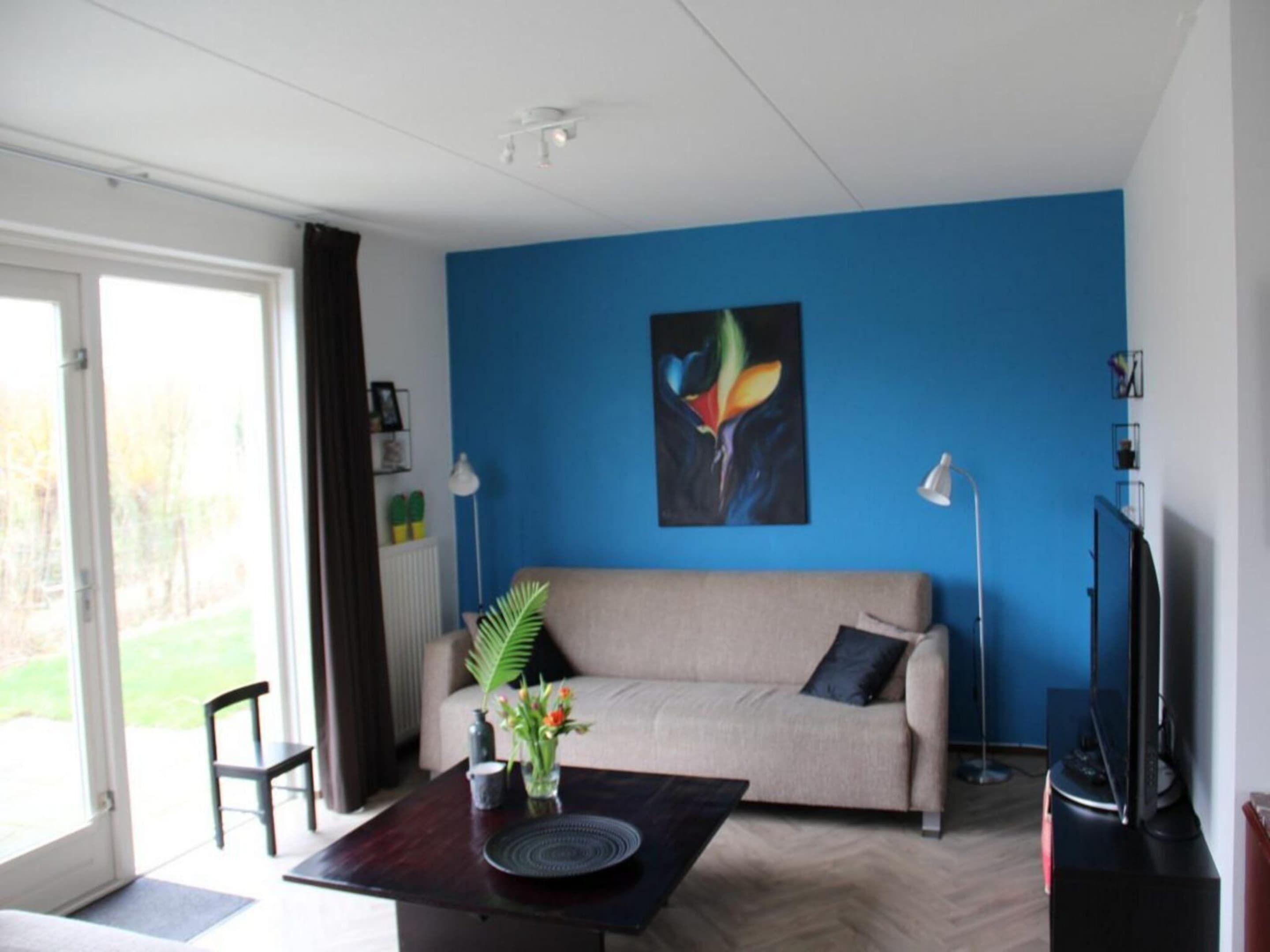 A living room with a beige sofa, a coffee table with a vase of flowers, a painting on the wall, and a television.