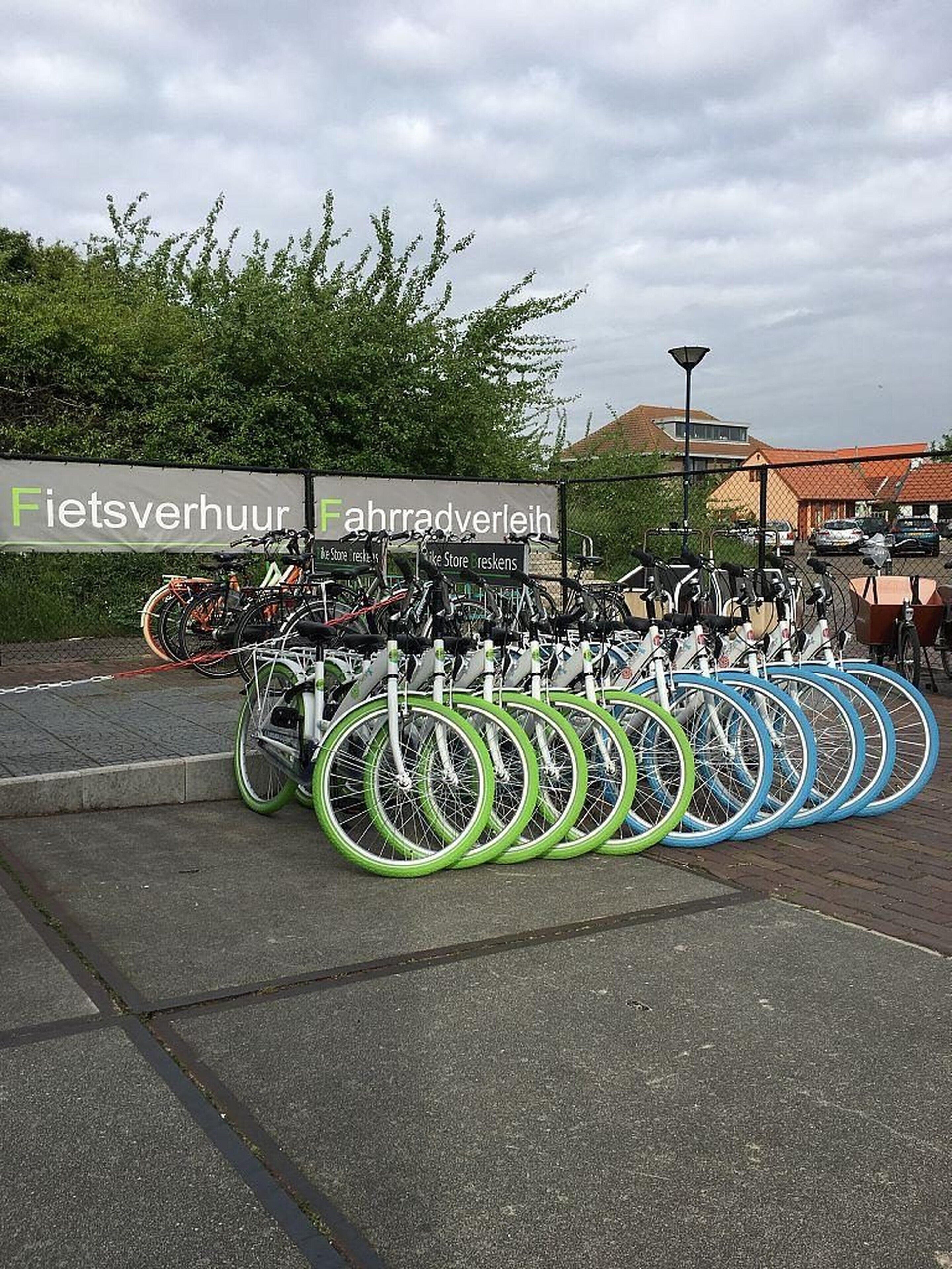A bicycle parking area with multiple bicycles and a sign in the background.