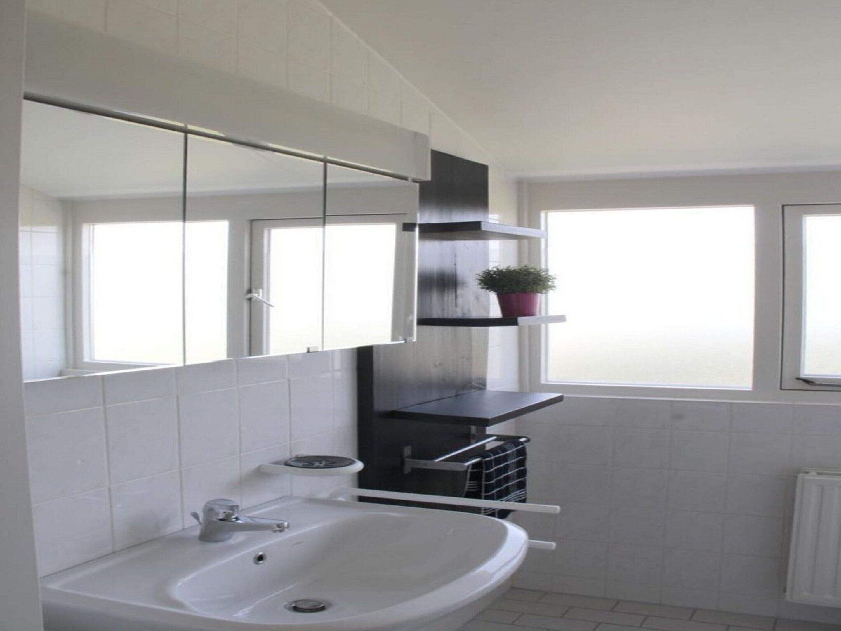 A modern bathroom with a white sink, a large mirror, and a window providing natural light.