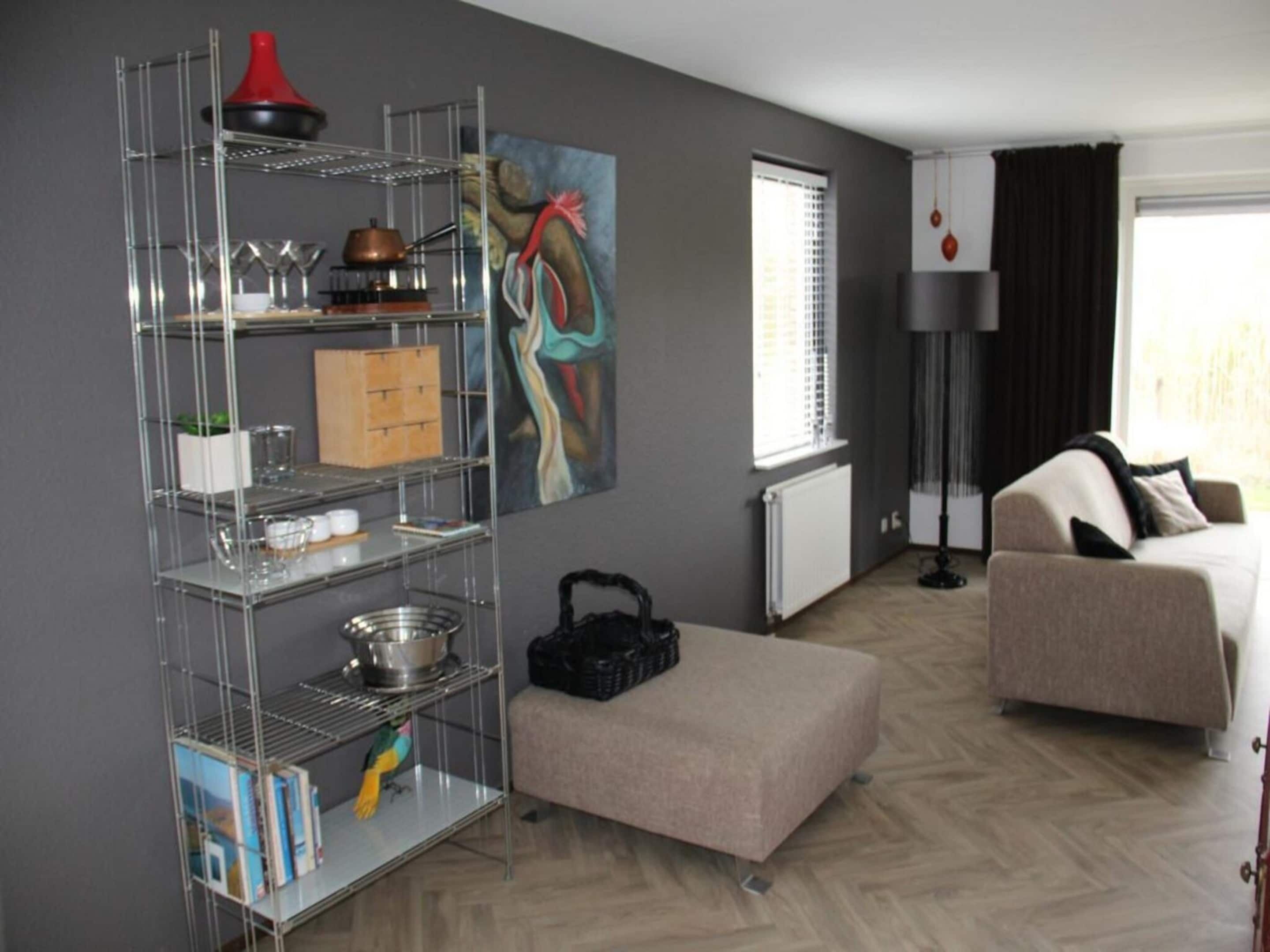 A hotel room with a kitchenette, a sofa, a painting, and a window with blinds.