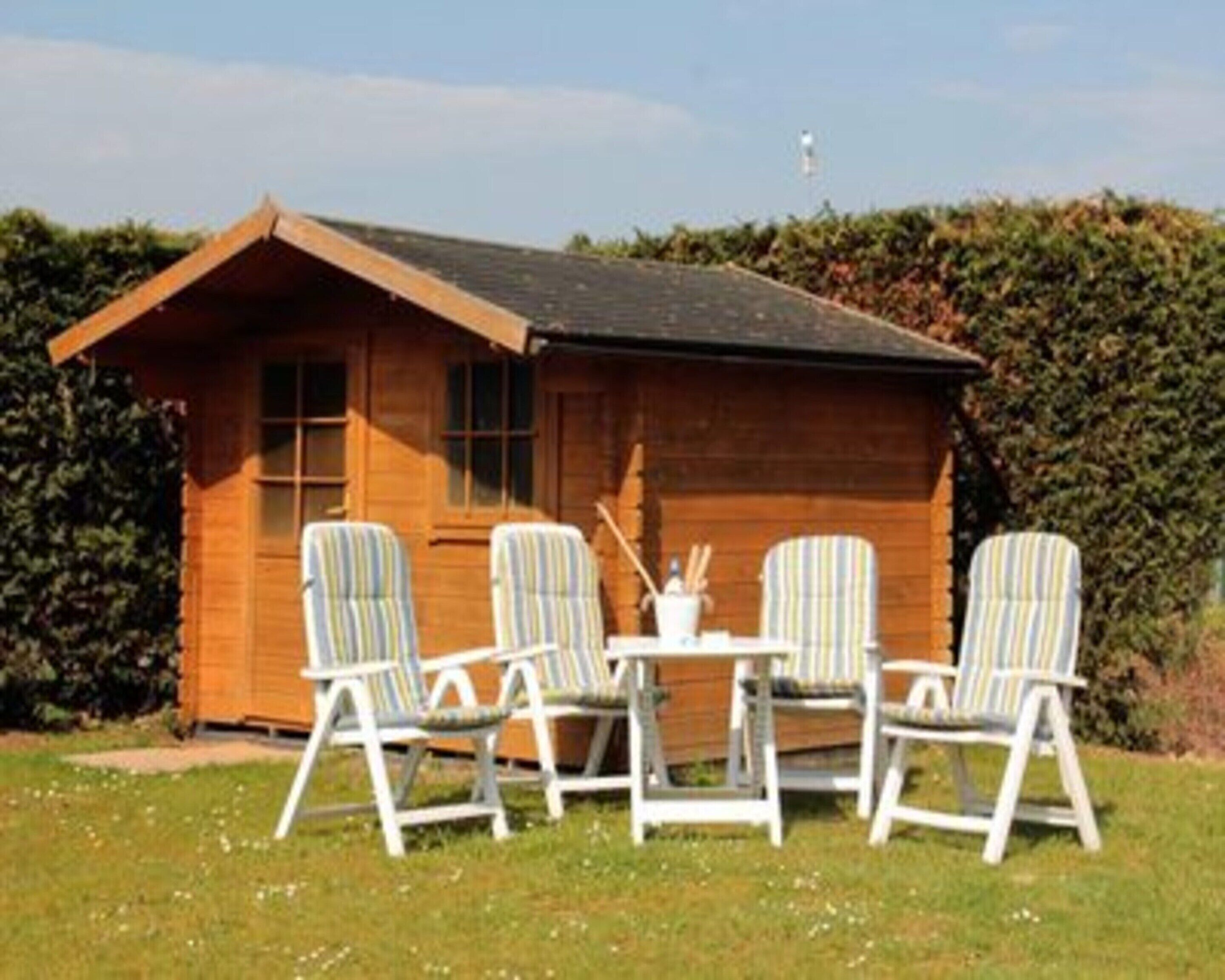 A wooden cabin with a sloped roof, four striped chairs, and a small table with a cup and spoon set.
