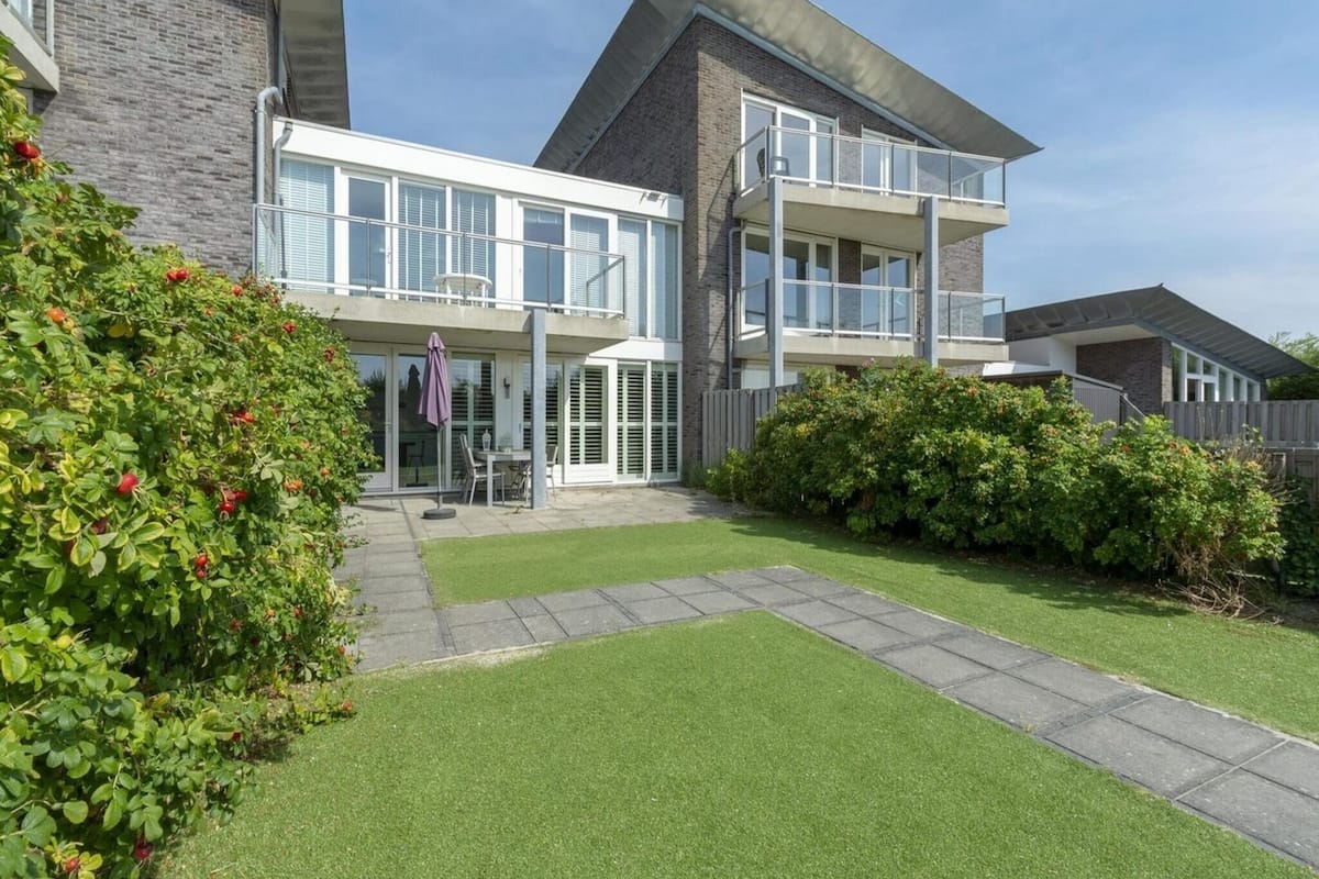 A modern two-story house with a balcony, a small patio, and a well-maintained lawn.