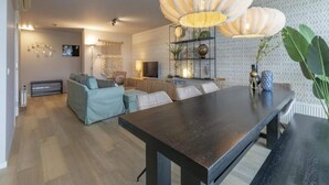 A modern living room with a dark wooden dining table, a light blue sofa, and a large potted plant. - Fantastic Apartment Seaside With Terrace (Callantsoog)