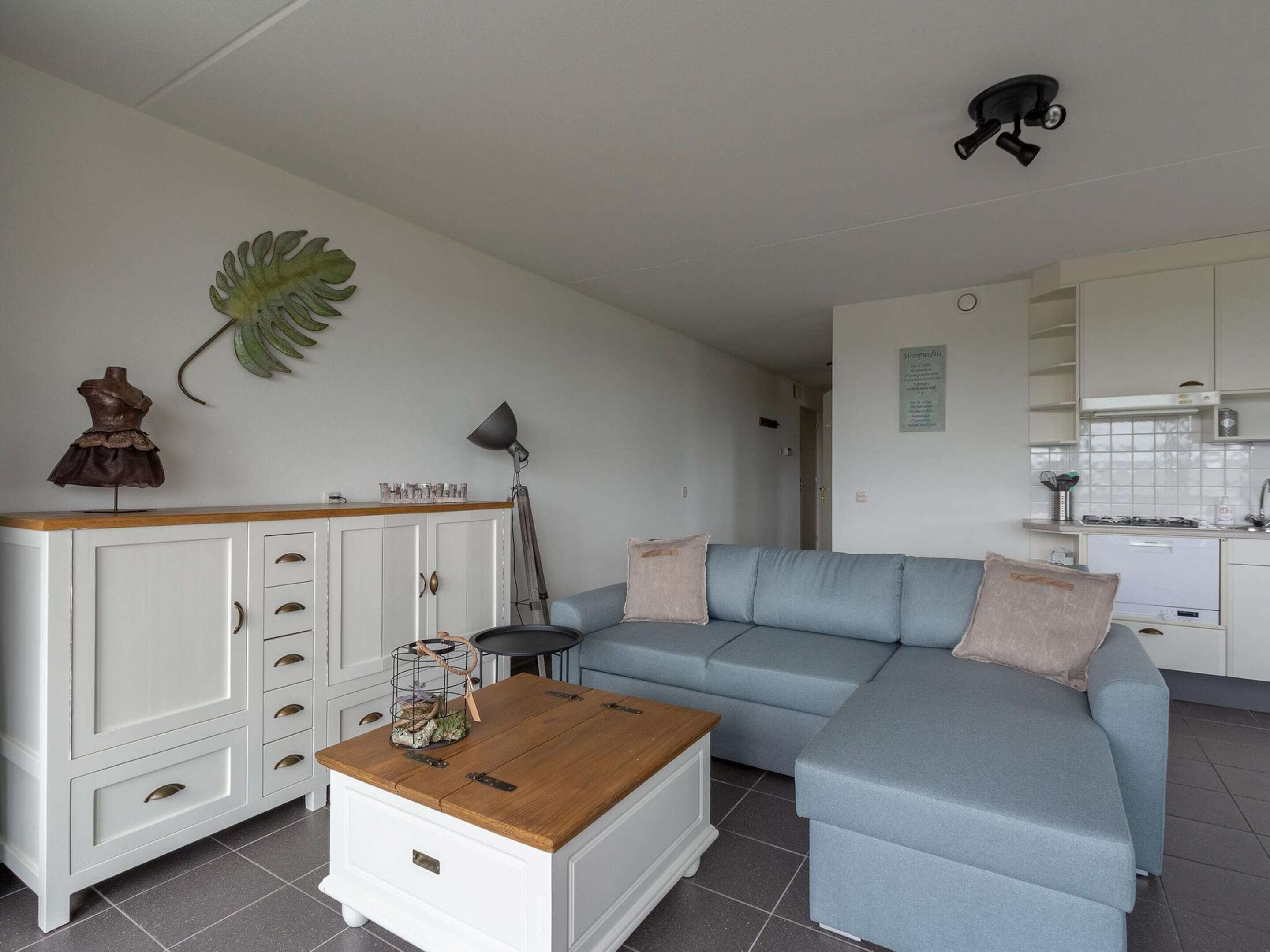 A living room with a sectional sofa, a white cabinet with drawers, a coffee table, a lamp, and a wall-mounted plant.