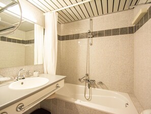 Een badkamer met een wastafel, spiegel, douche en betegelde wanden.
