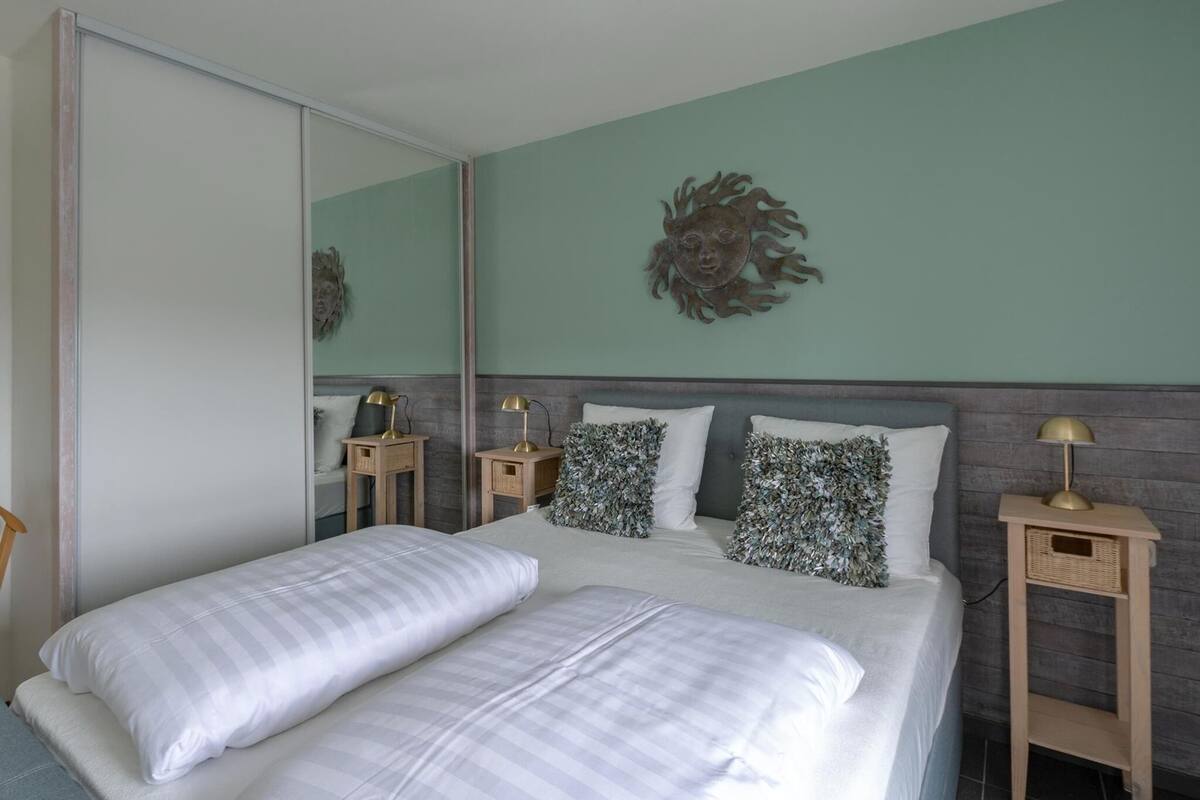 Un dormitorio con dos camas, un espejo grande, un cuadro decorativo de un sol y lámparas de noche.