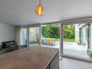 Et moderne køkken med en stor ø, skydedøre til en terrasse med bord og stole, samt en hængende lampe.