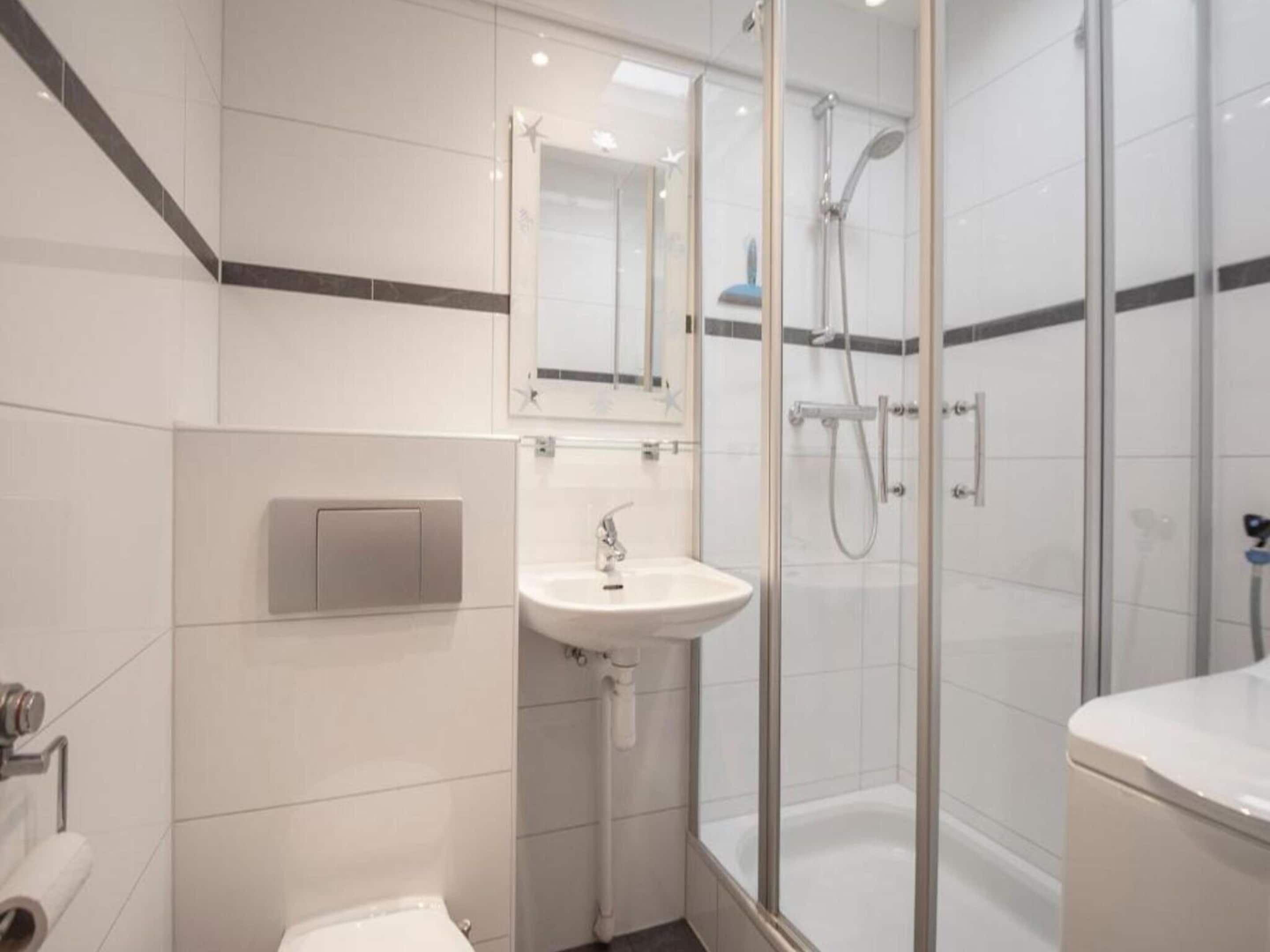 A modern bathroom with a glass-enclosed shower, a pedestal sink, and a toilet.