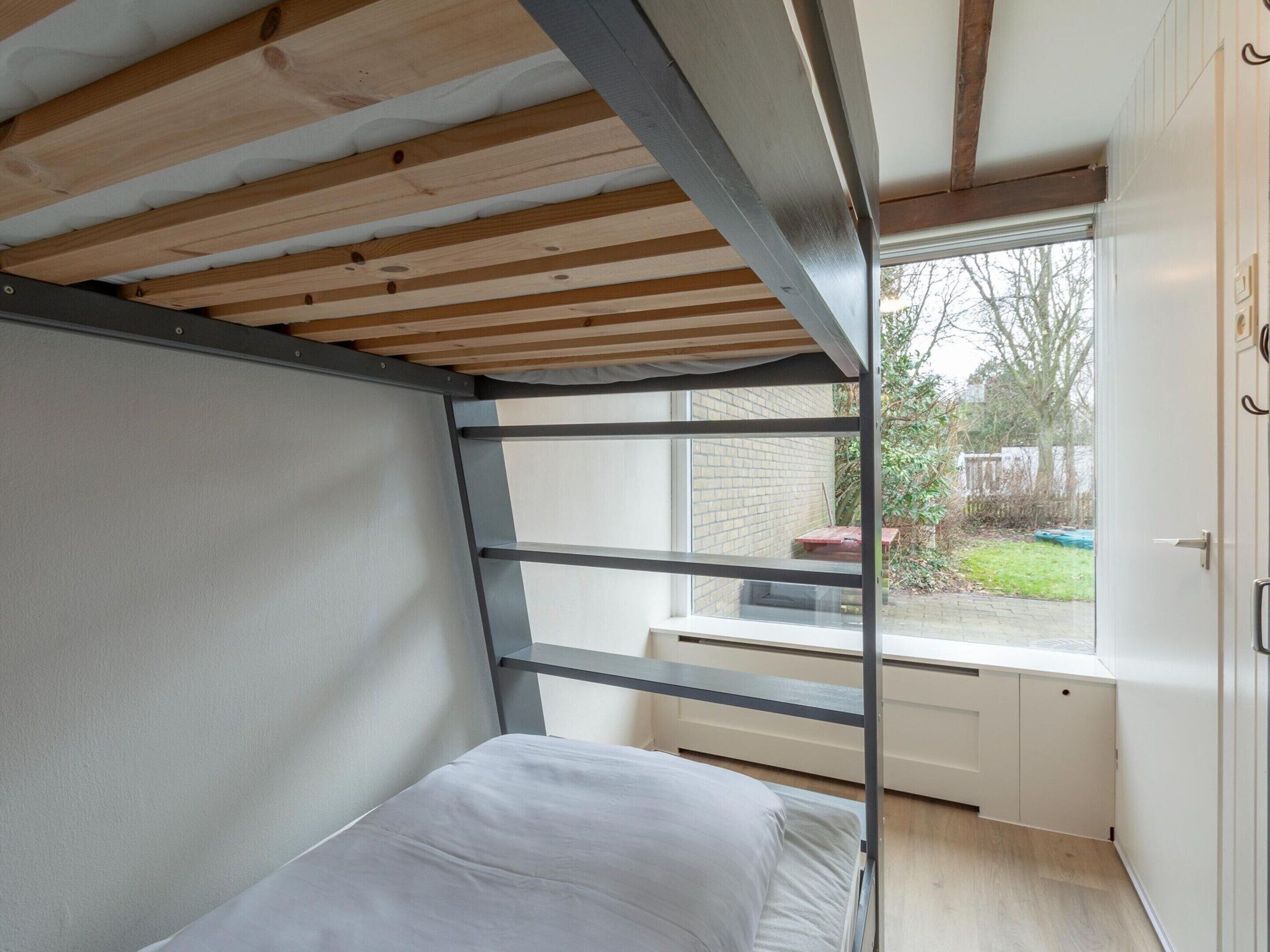 A compact room with a bunk bed, a window with a view of a garden, and a door with a handle.