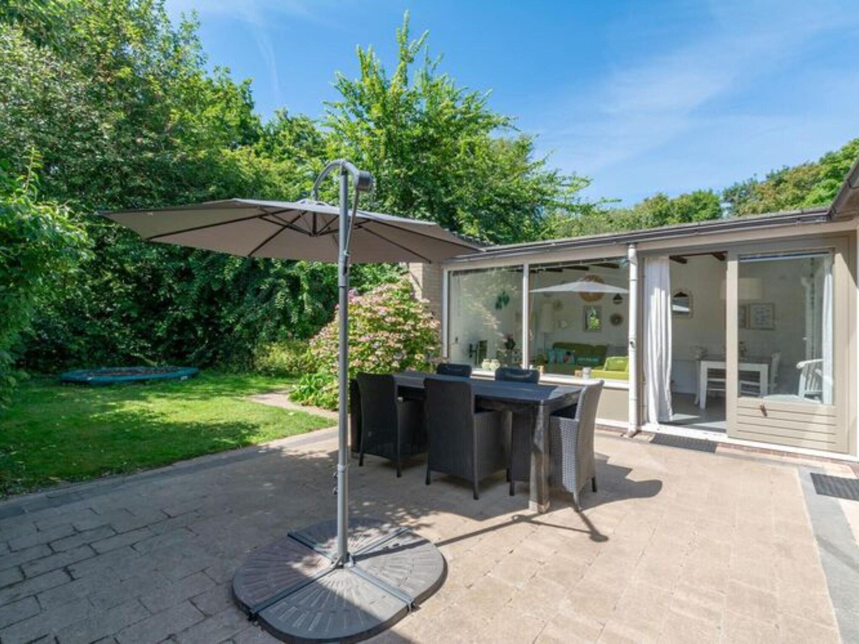 An outdoor patio with a table and chairs, a covered umbrella, and a glass-enclosed room with a view of the garden.