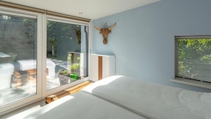 Ein Schlafzimmer mit einer großen Schiebeglasdoor zum Balkon, einem Bett mit weißer Matratze, einem Wandradiator und einer Stierkopf-Dekoration.