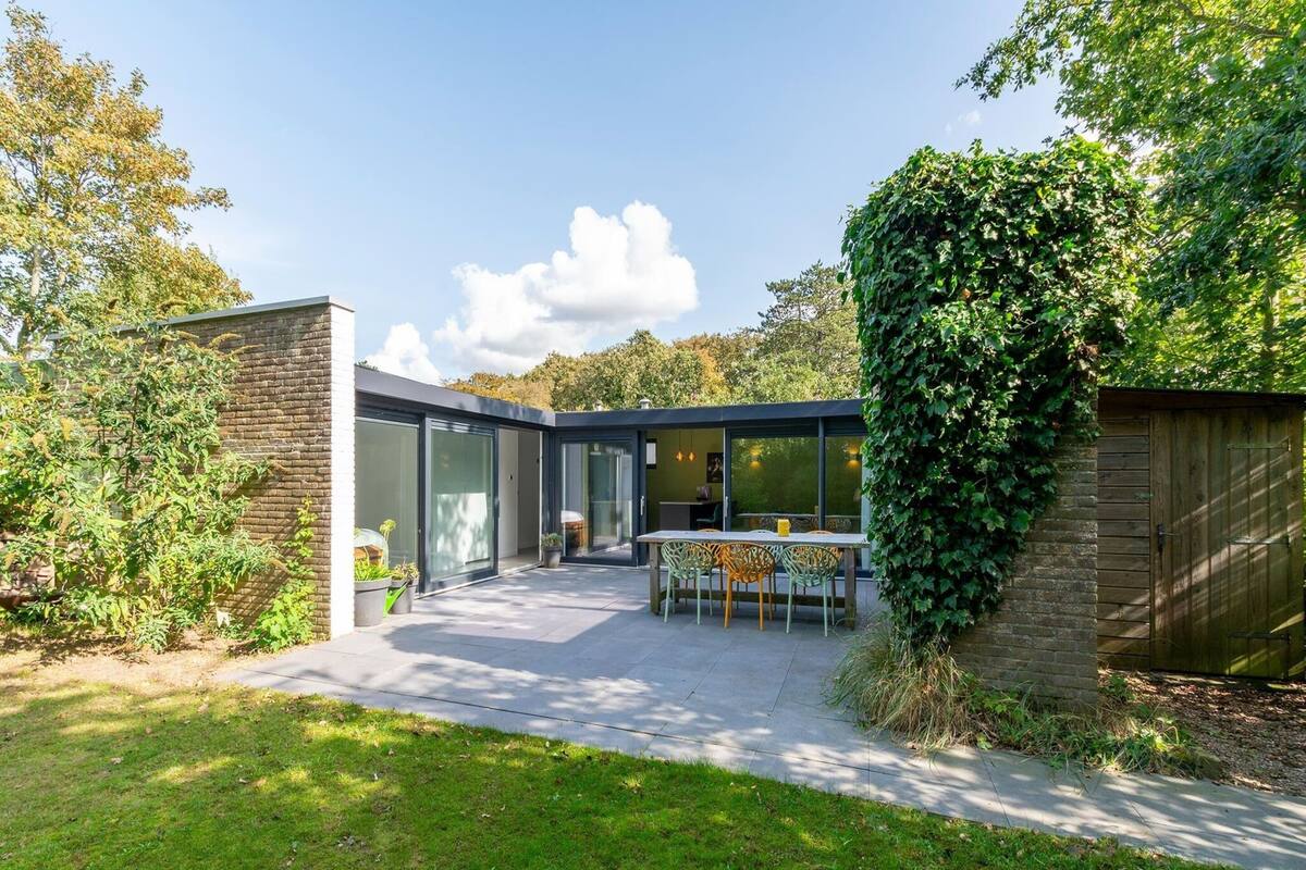 A modern house with a patio, a dining area, and a large glass door leading to a garden.