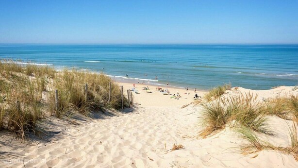 Ein sandiger Strand mit blauem Himmel und ruhigem Meer.