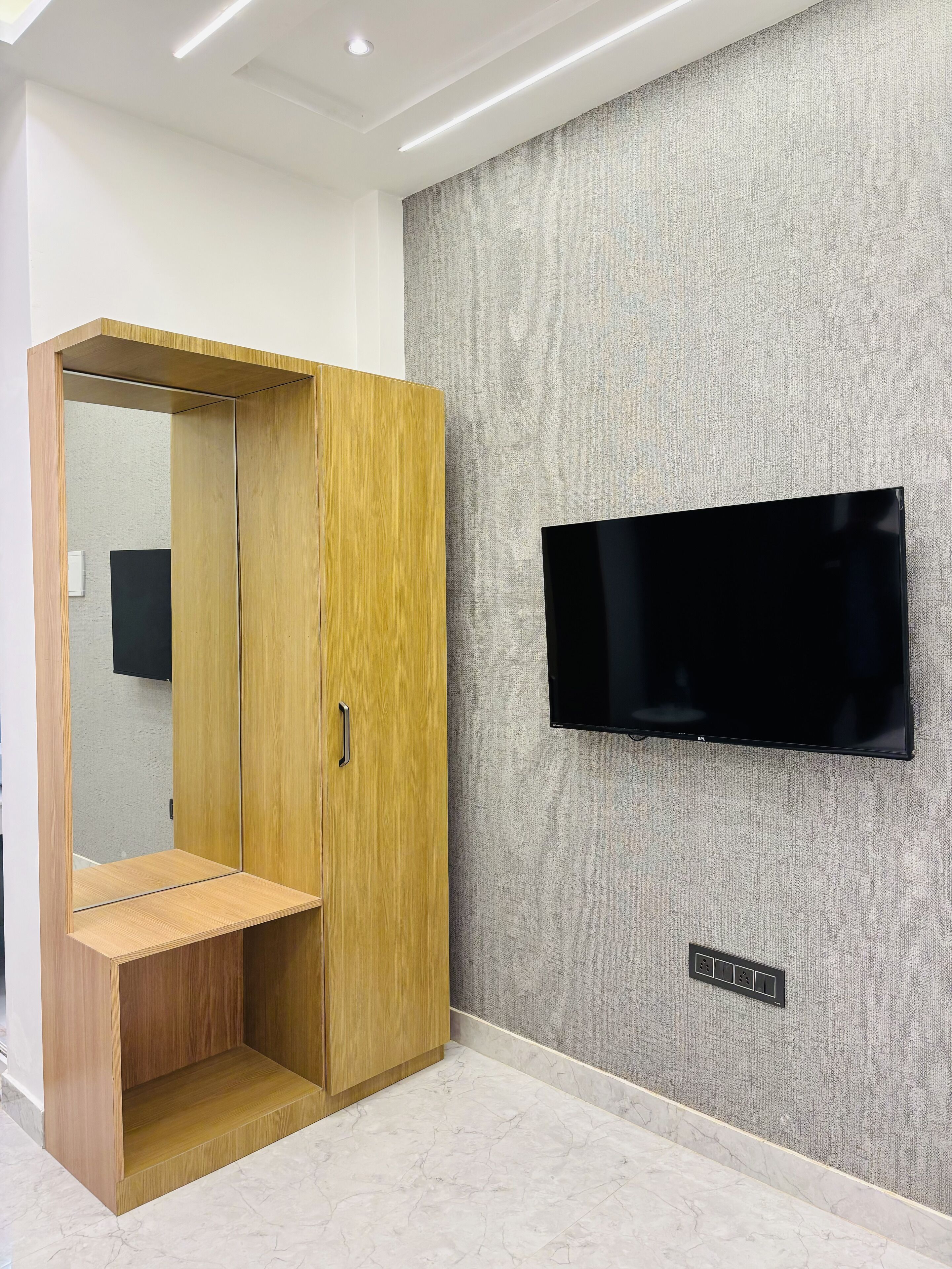 A room with a wooden wardrobe, a flat-screen TV mounted on the wall, and a marble floor.