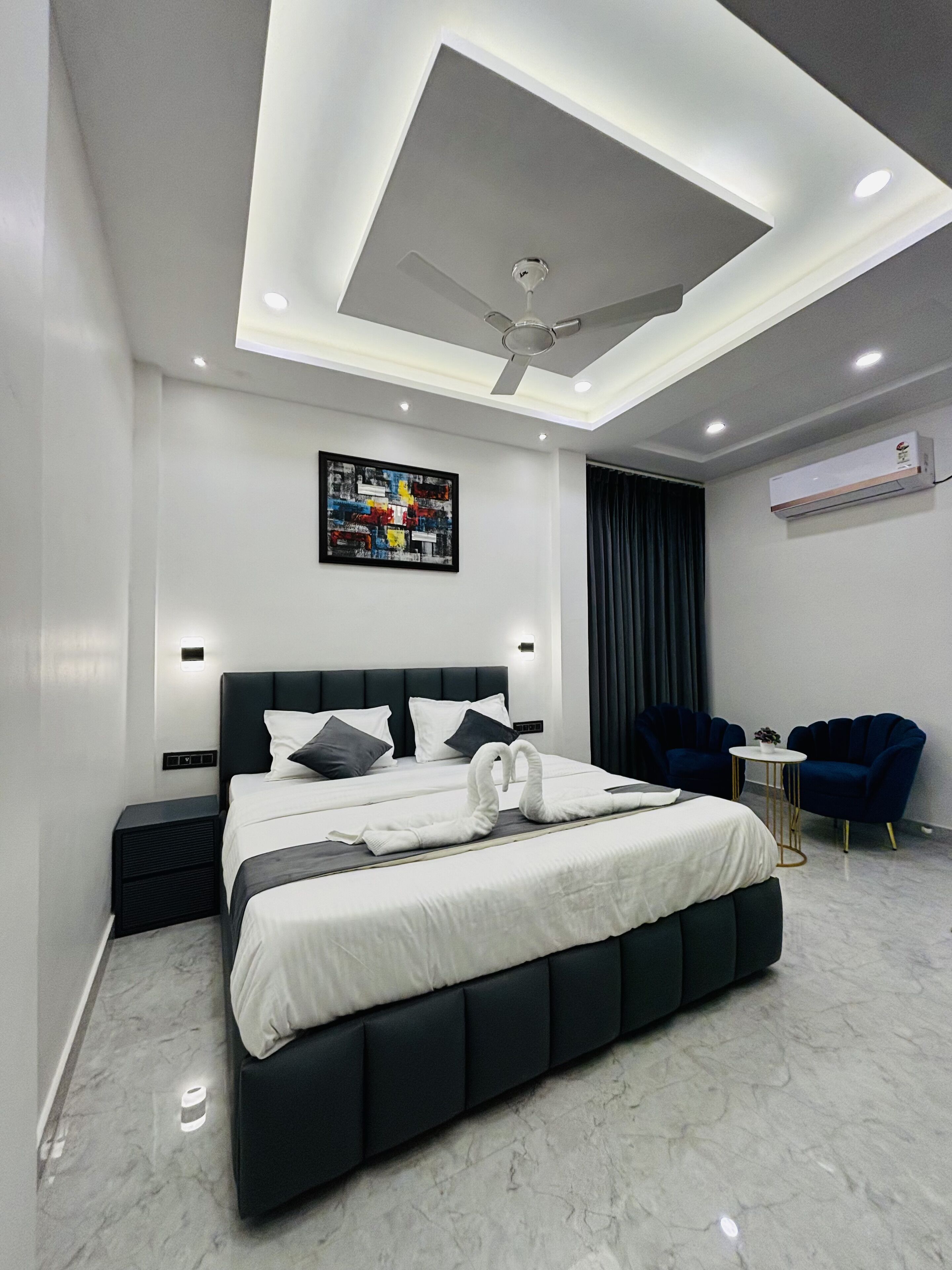 Un dormitorio moderno con una cama grande, un ventilador de techo, un equipo de aire acondicionado y una pequeña mesa con sillas.