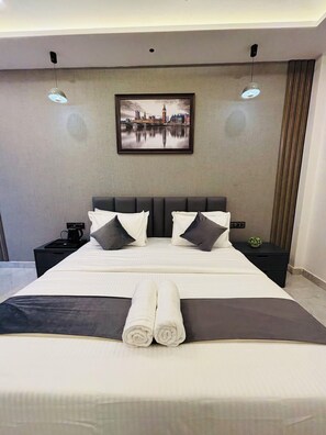 A modern hotel room with a large bed, two bedside tables, a coffee maker, and a framed cityscape picture on the wall.