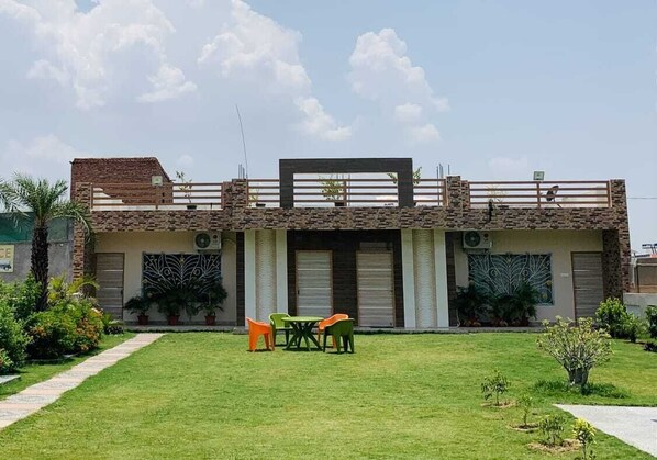 Un bâtiment à deux étages, doté d’un toit plat, d’un balcon et d’un petit jardin avec une table et des chaises.