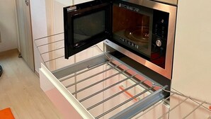 Une cuisine compacte équipée d’un four à micro-ondes, d’un appareil rouge posé sur une étagère et d’un vaporisateur.