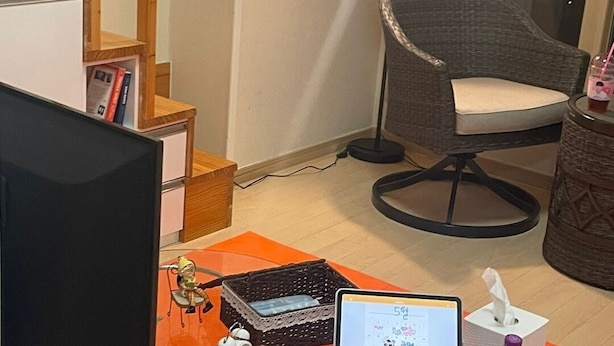 Une pièce avec une table en verre, un ordinateur portable, une lampe, une chaise et un escalier.