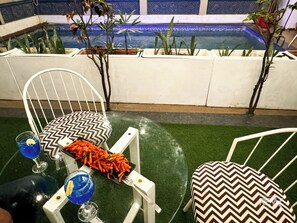 A poolside seating area with a glass table, two chairs, a tray of food, and two drinks. - The Wraveler Tapovan Rooms and Dorms (Rishikesh)