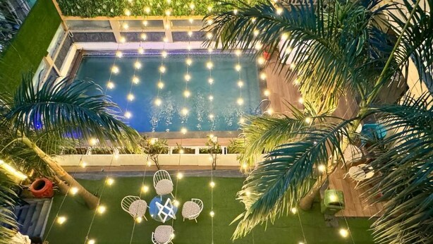Un área de piscina con luces colgantes, palmeras y mobiliario exterior.