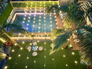 A pool area with string lights, palm trees, and outdoor seating. - The Wraveler Tapovan Rooms and Dorms (Rishikesh)