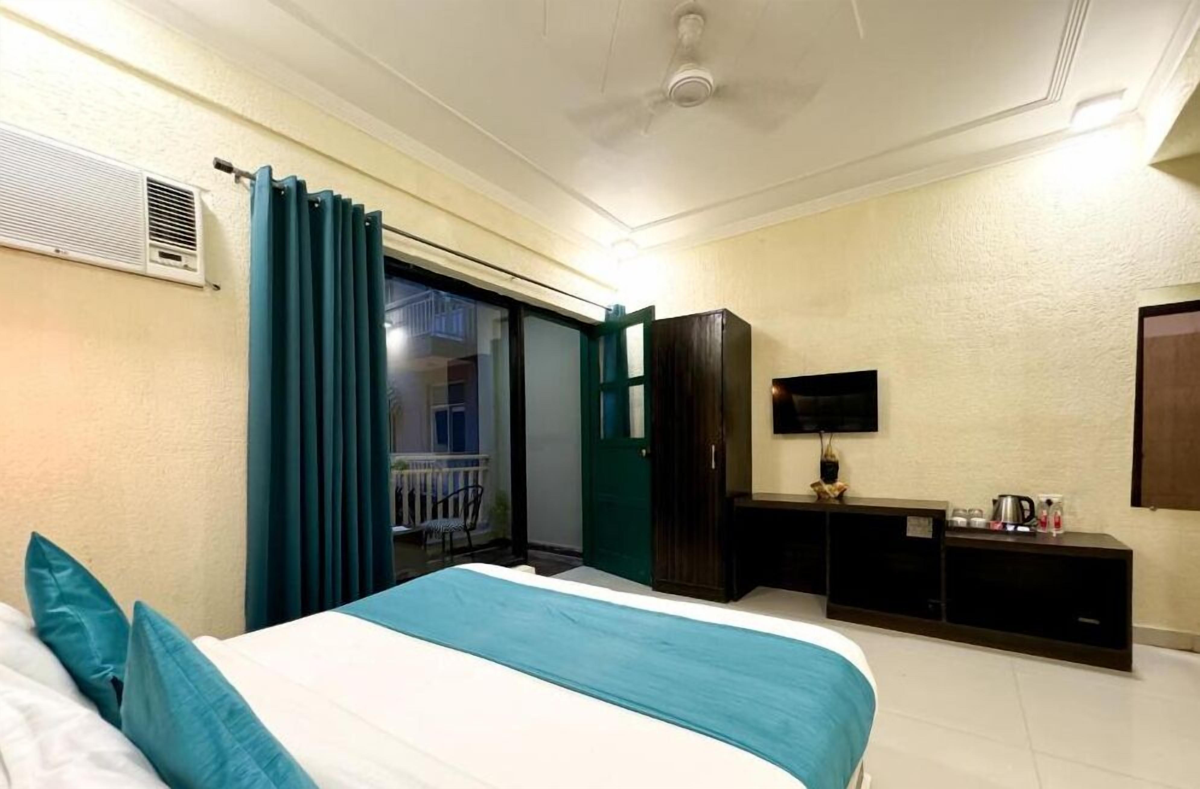 A hotel room with a bed, a desk, a television, and a sliding door to a balcony.