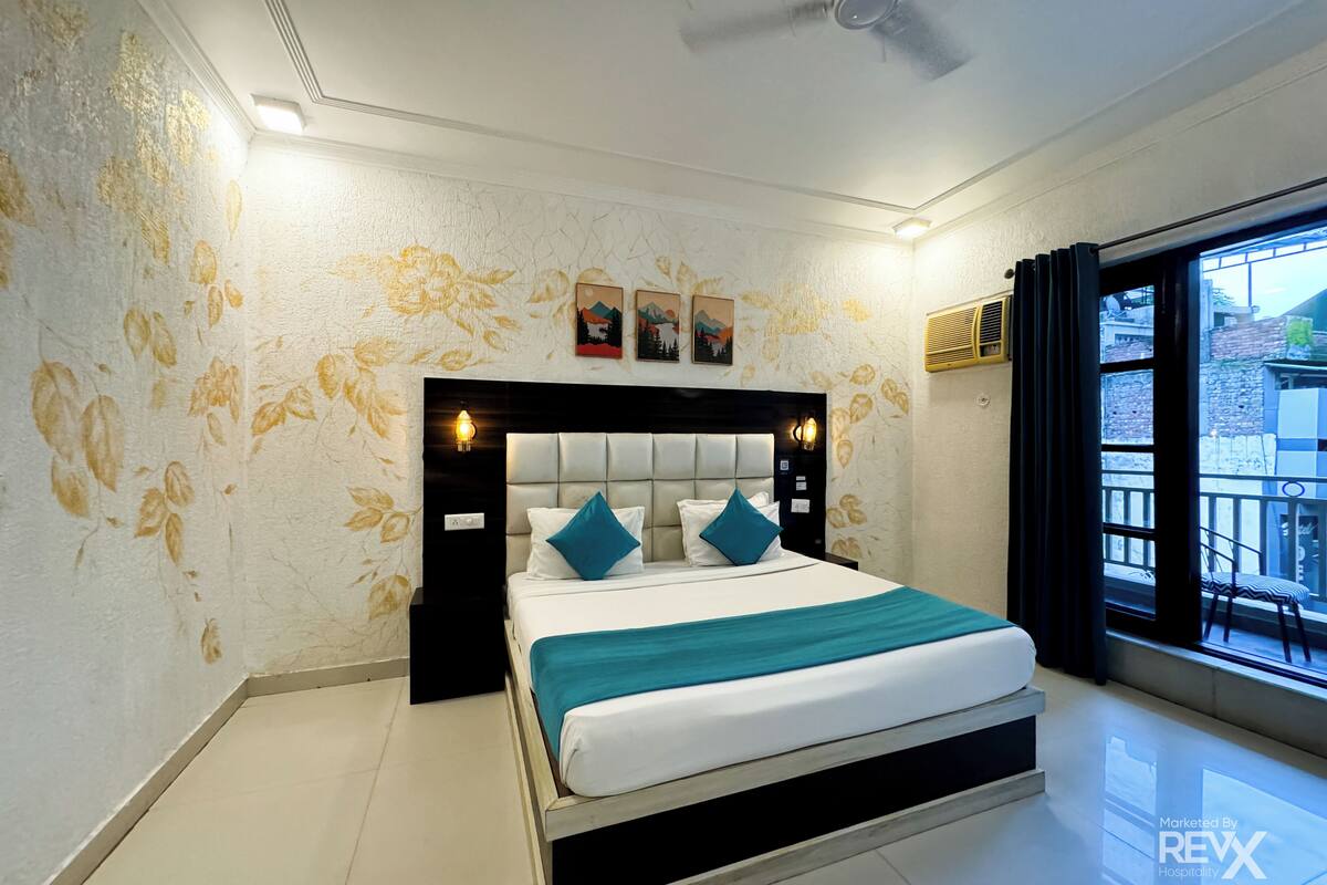 A hotel room with a bed, a ceiling fan, and a window with a view of buildings outside.