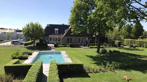 Ein Wohnhaus mit Swimmingpool, gepflegtem Rasen und einem großen Gebäude mit dunklem Dach.