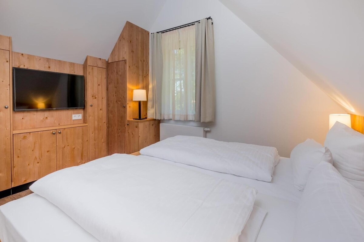 A bedroom with a bed, wooden paneling, a TV, and two bedside lamps.