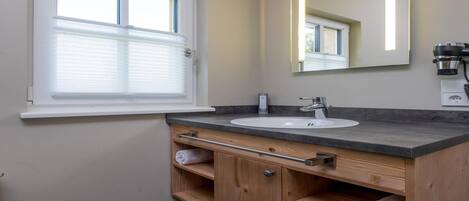 A bathroom with a window, a sink, a mirror, and wooden cabinets.