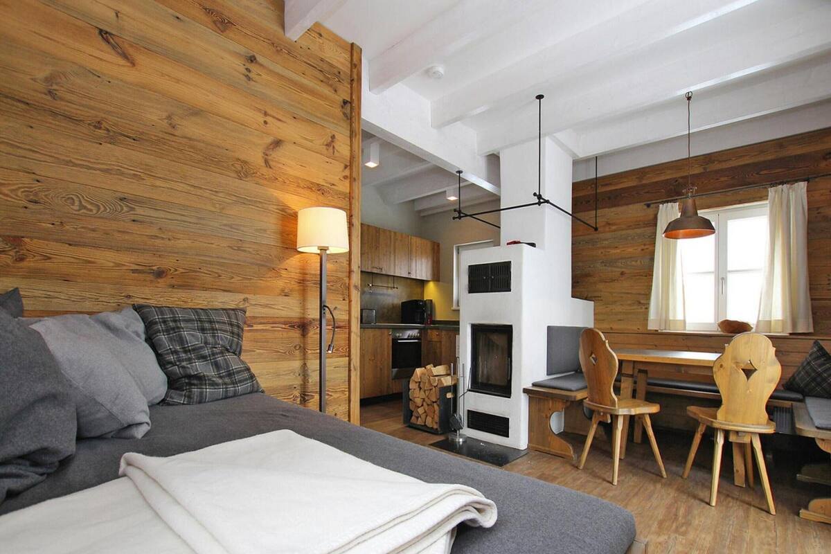 A cozy room with a bed, a wooden wall, a kitchen area, and a dining table with chairs.