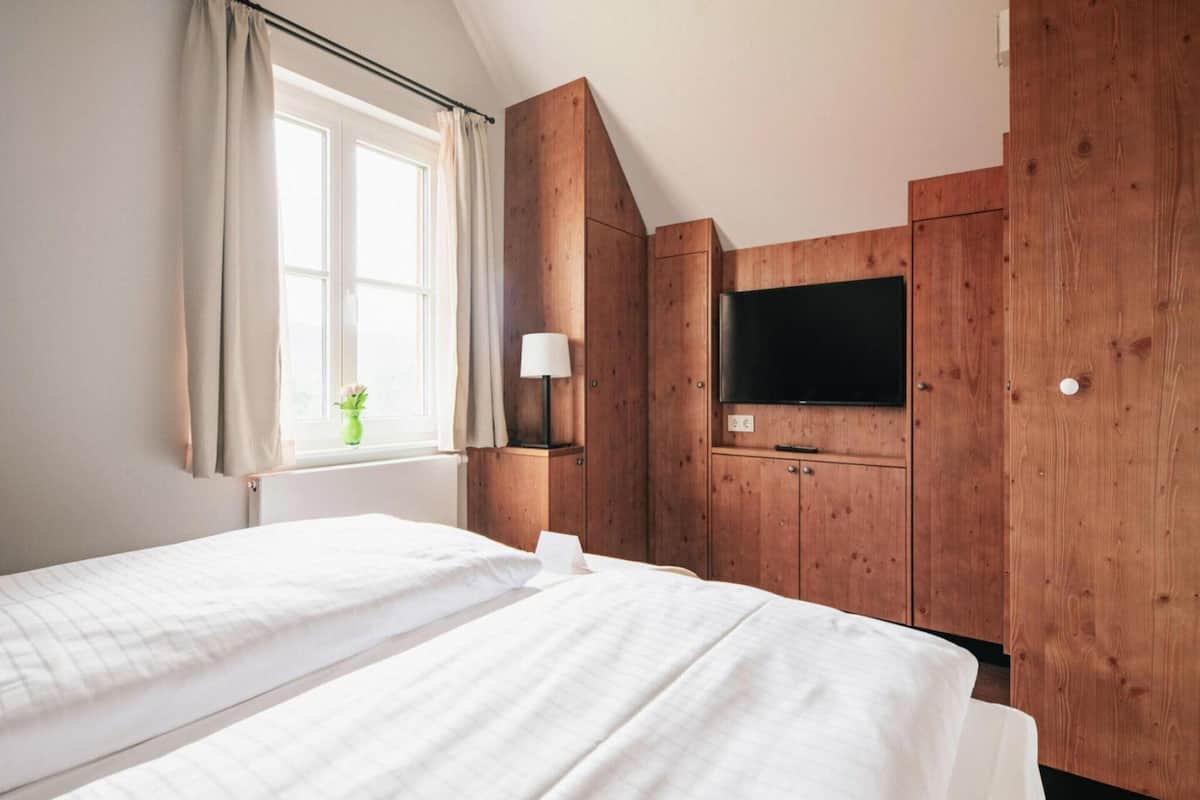 A bedroom with two beds, a TV, wooden cabinets, and a window with curtains.