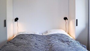 A bedroom with a bed, two black wall-mounted lamps, and white wardrobes. - 4 Person Holiday Home in Ronne (Ronne)