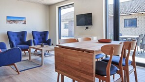 A modern living room with a wooden dining table, blue armchairs, and a TV mounted on the wall. - 4 Person Holiday Home in Ronne (Ronne)