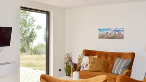 A modern living room with a sofa and chairs, a flat-screen TV, and a painting on the wall. - 4 Person Holiday Home in Ronne (Ronne)