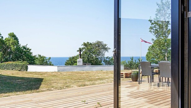 A wooden deck with a view of the sea, outdoor furniture, and a flag. - 4 Person Holiday Home in Ronne (Ronne)