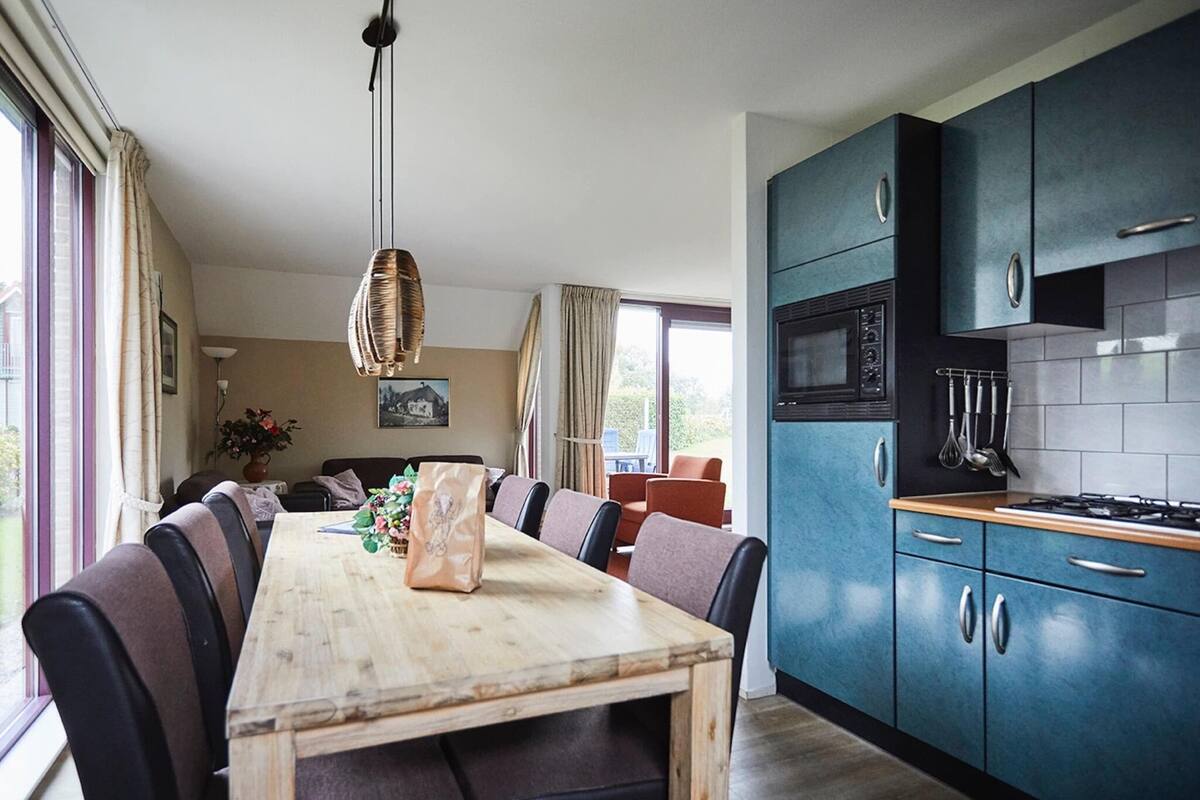 Une cuisine moderne avec des meubles de couleur turquoise, une table à manger en bois et un luminaire suspendu.